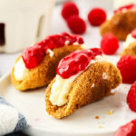 cheesecake tacos on a plate surrounded by fresh raspberries and a blue and white napkin